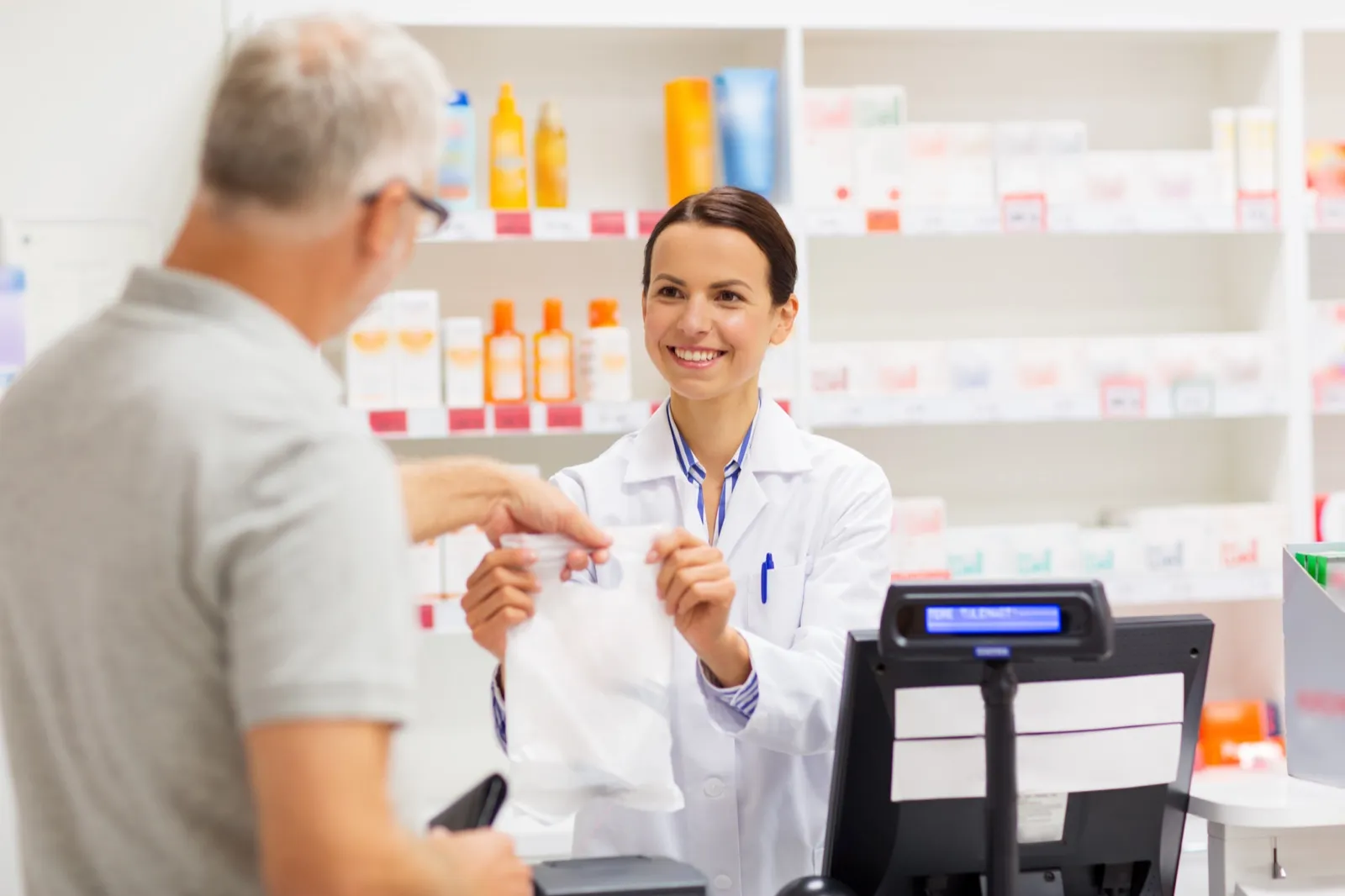 A pharmacist handing a filled prescription to a customer at the counter